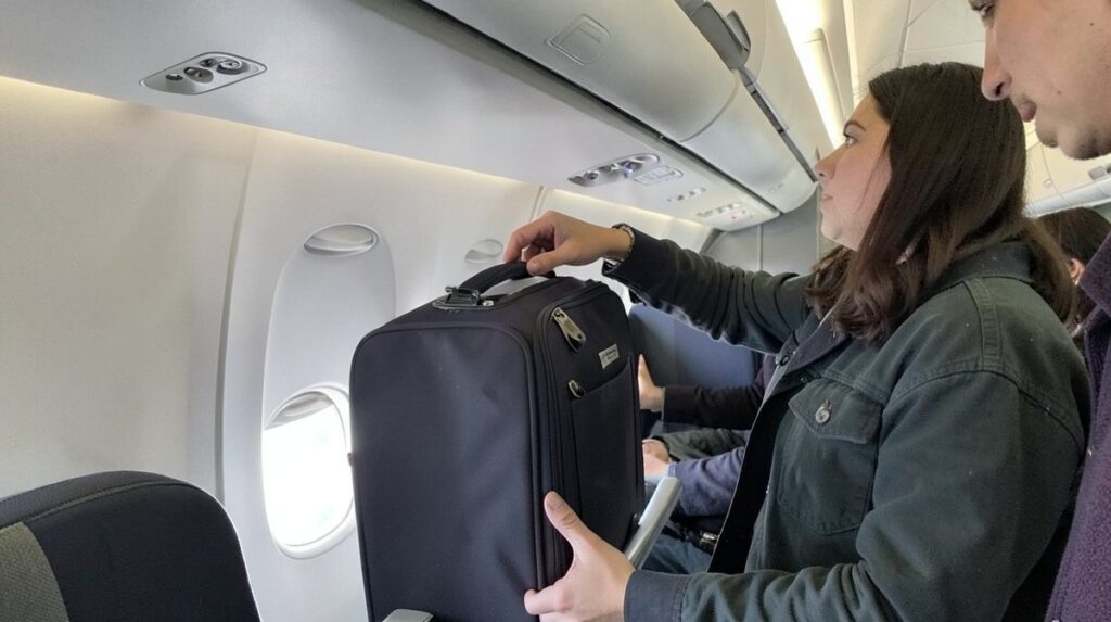 Bagage cabine Corsair : un voyageur range sa valise cabine dans le coffre à bagages de l'avion